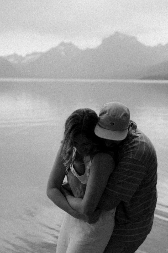 couple hugs in front of mountains at lake mcdonald
