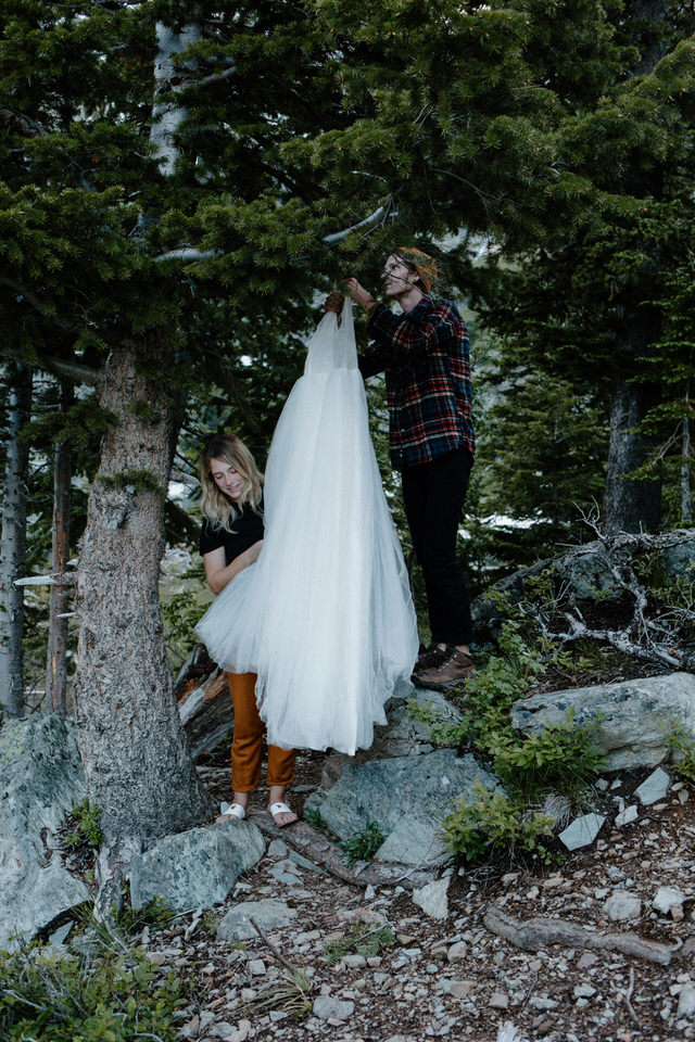 bride and groom hangs wedding dress in mountain trees